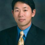 headshot of Asian male doctor, wearing black blazer, blue shirt and gold tie