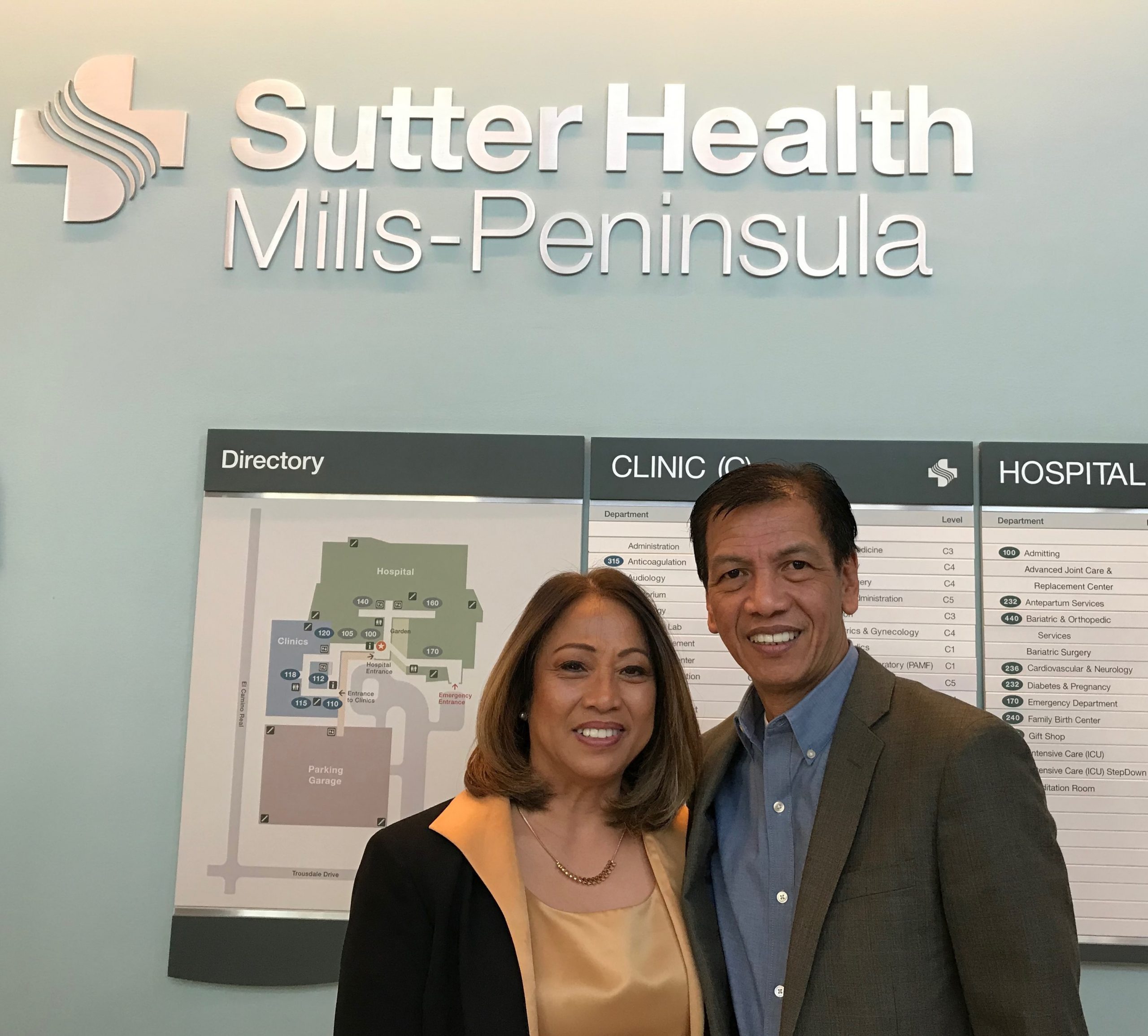 Wife and stroke survivor husband under sign for Sutter Health Mills-Peninsula.