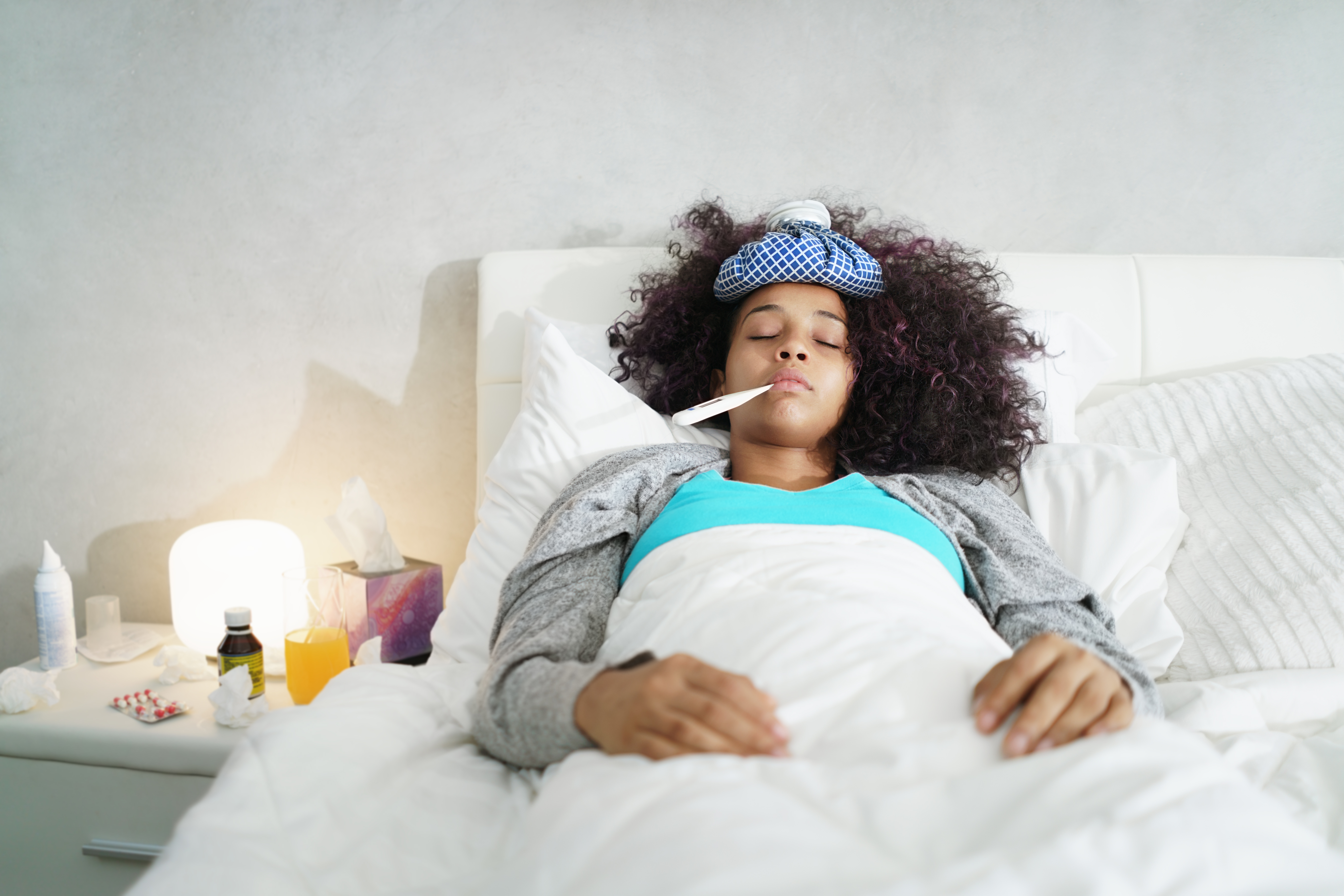 Woman With Fever Using Thermometer And Resting in Bed