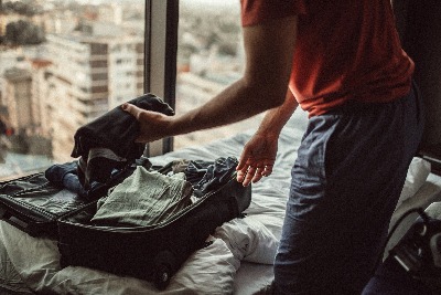 Man unpacking suitcase on a bed in front of large window looking onto a cityscape