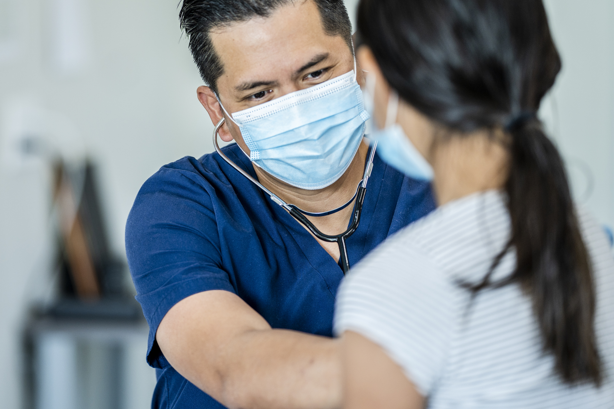 Clinician with mask examines female pediatric patient