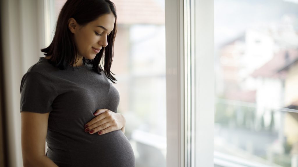 Pregnant Latina woman standing beside window