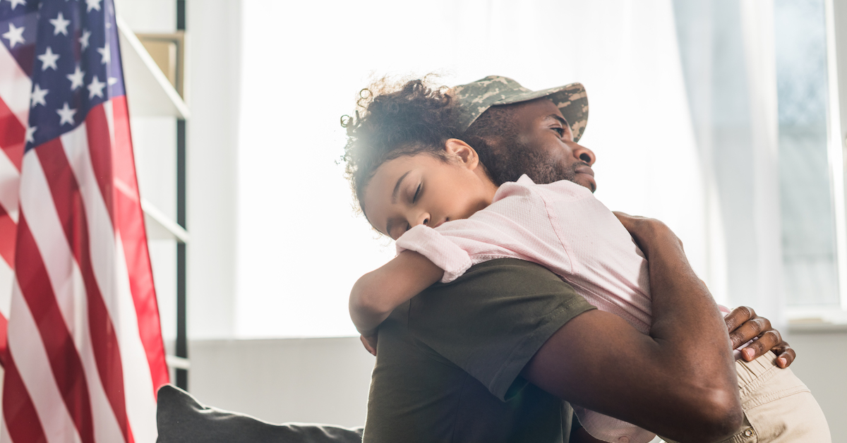 Male soldier in camouflage clothes and her daughter embracing on sofa