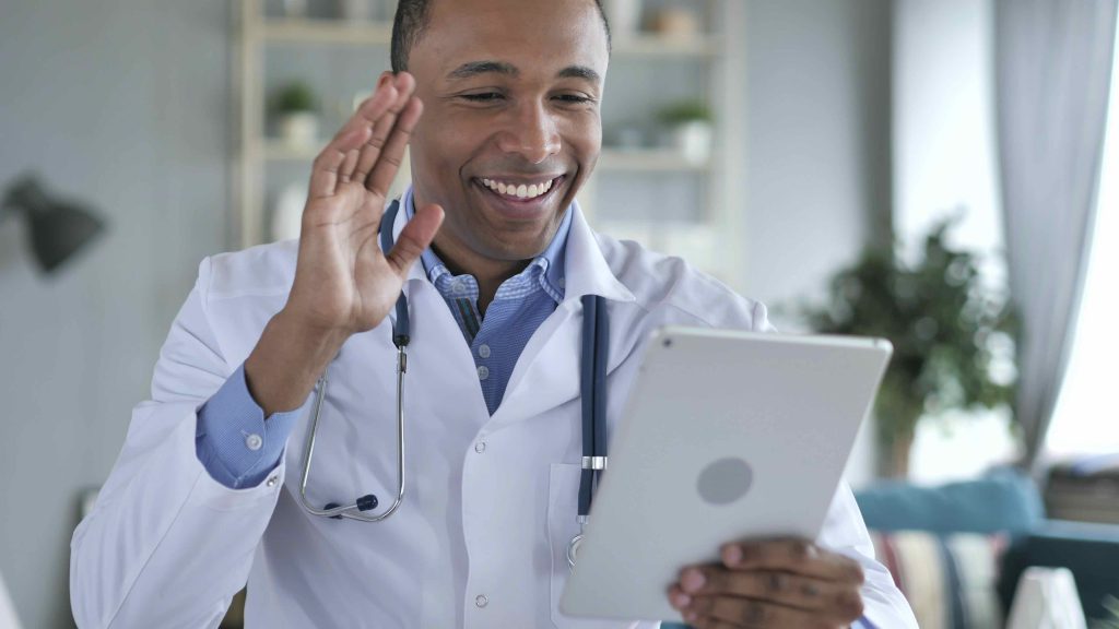 A doctor using a tablet and waving at his patients during a virtual care session