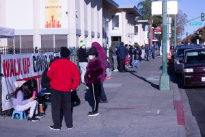 People standing in line down a city street and around a building waiting for COVID-19 testing