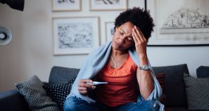 Worried Black woman sitting on a couch, feeling symptoms.