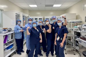 Seven women in full scrubs and PPE pose in an operating room ahead of Christine valve surgery.