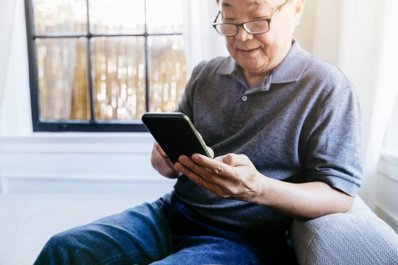 Active Asian senior man concentrates while texting on his phone