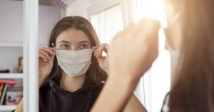 young girl wearing medical protective face mask looking mirror