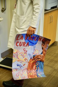 Doctor holds colorful 'La vacuna cura' poster