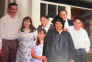 Latina woman in graduation cap and gown poses with her family