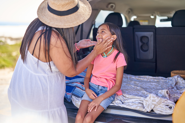 Affectionate mother applying sunscreen to daughter at back of car