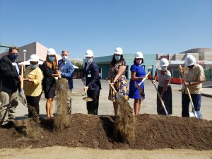 Various people with hardhats and shovels break ceremonial ground in hospital parking lot
