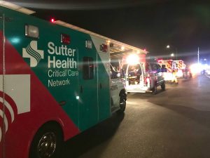 Sutter Health branded ambulances line up on sidewalk in the middle of the night with EMS personnel