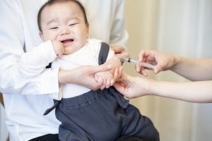 Photo of a baby over 6 months old receiving a shot in the arm.