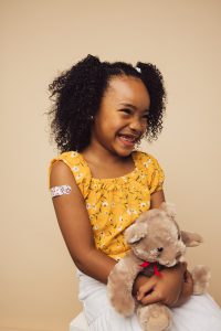 Photo of a child with band aid on her arm, holding teddy bear.
