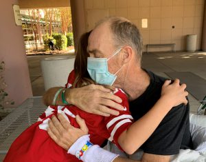 Young girl hugging her father who is in a wheelchair wearing a surgical mask