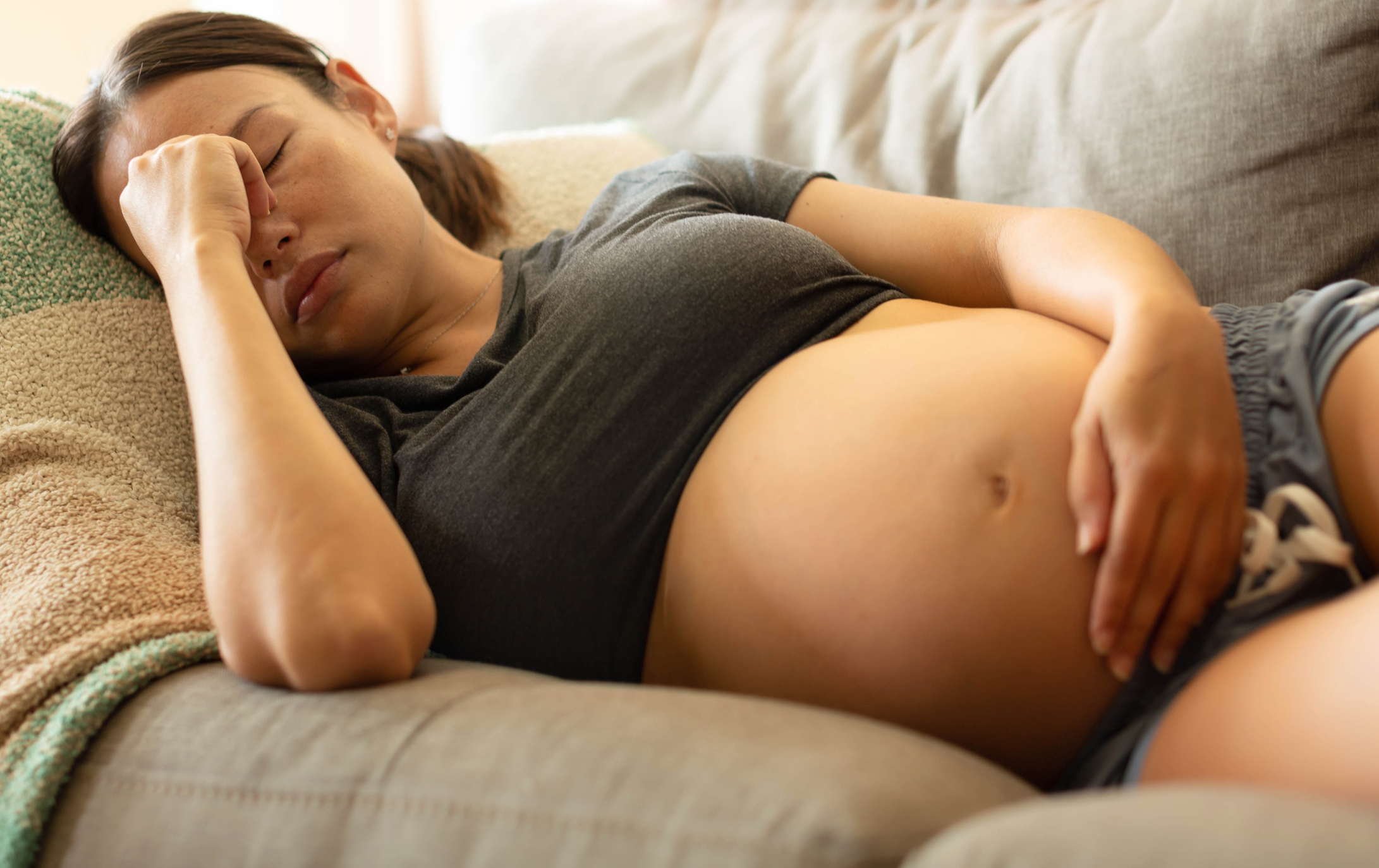 A uncomfortable pregnant mother trying to rest at home, lying on her couch holding her head.