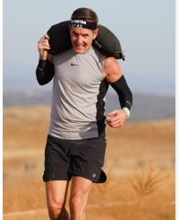 Caucasian male running with headband on and sandbag over his shoulder