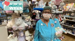 Alyce Glazer stands in a Sutter hospital giftshop holding a stuffed animal. She has short gray heir an dis wearing a white mask and a teal shirt.