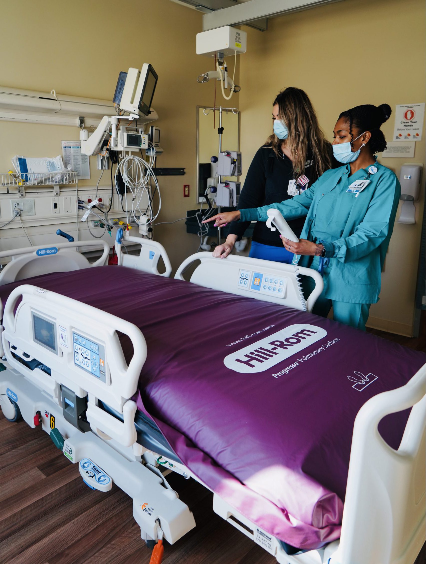 Two ICU nurses in masks stand with a new hospital smart bed