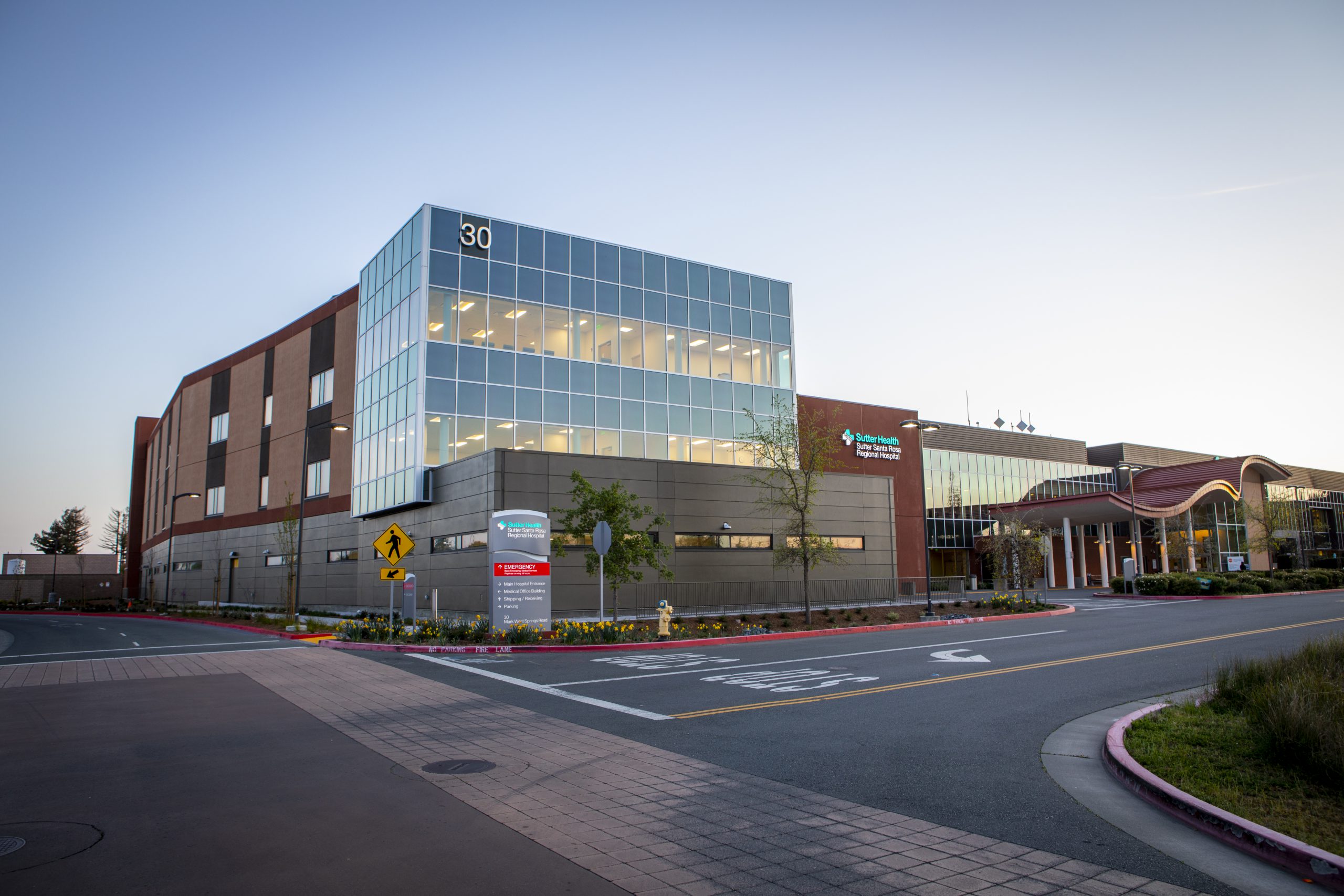 Santa Rosa Regional Hospital new three-story expansion tower is pictured at dusk with lights on inside the building, which features an all glass front.