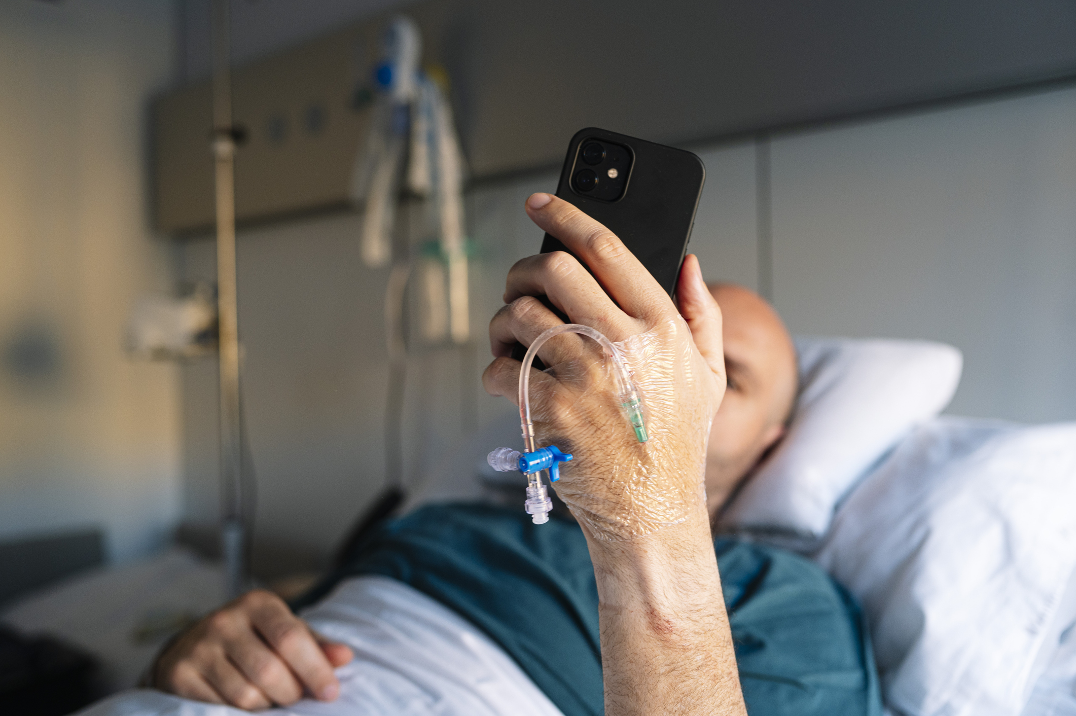 Caucasian male patient resting in hospital bed looking at his smartphone