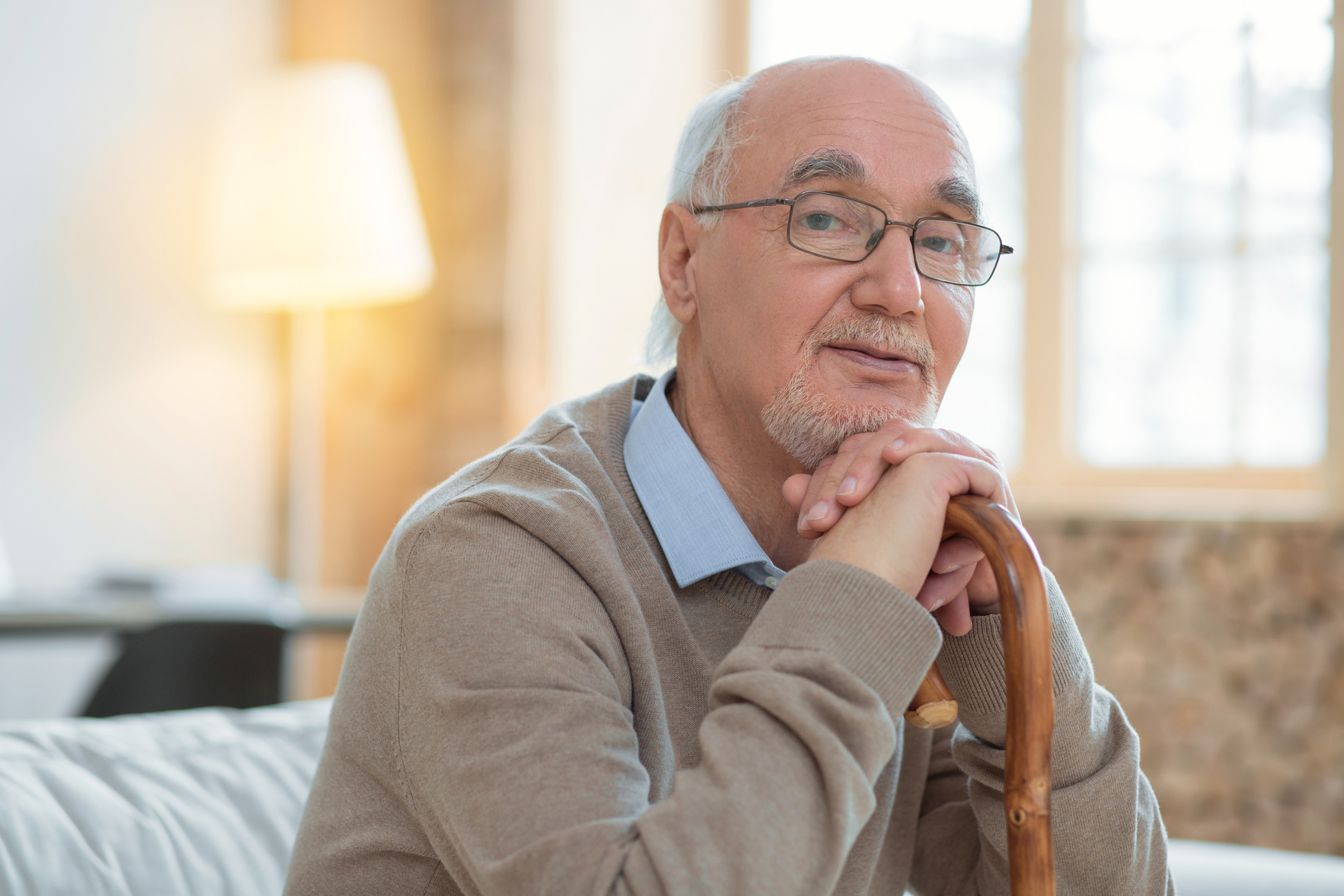 Meditative attractive senior man leaning on cane while wearing glasses and looking at camera