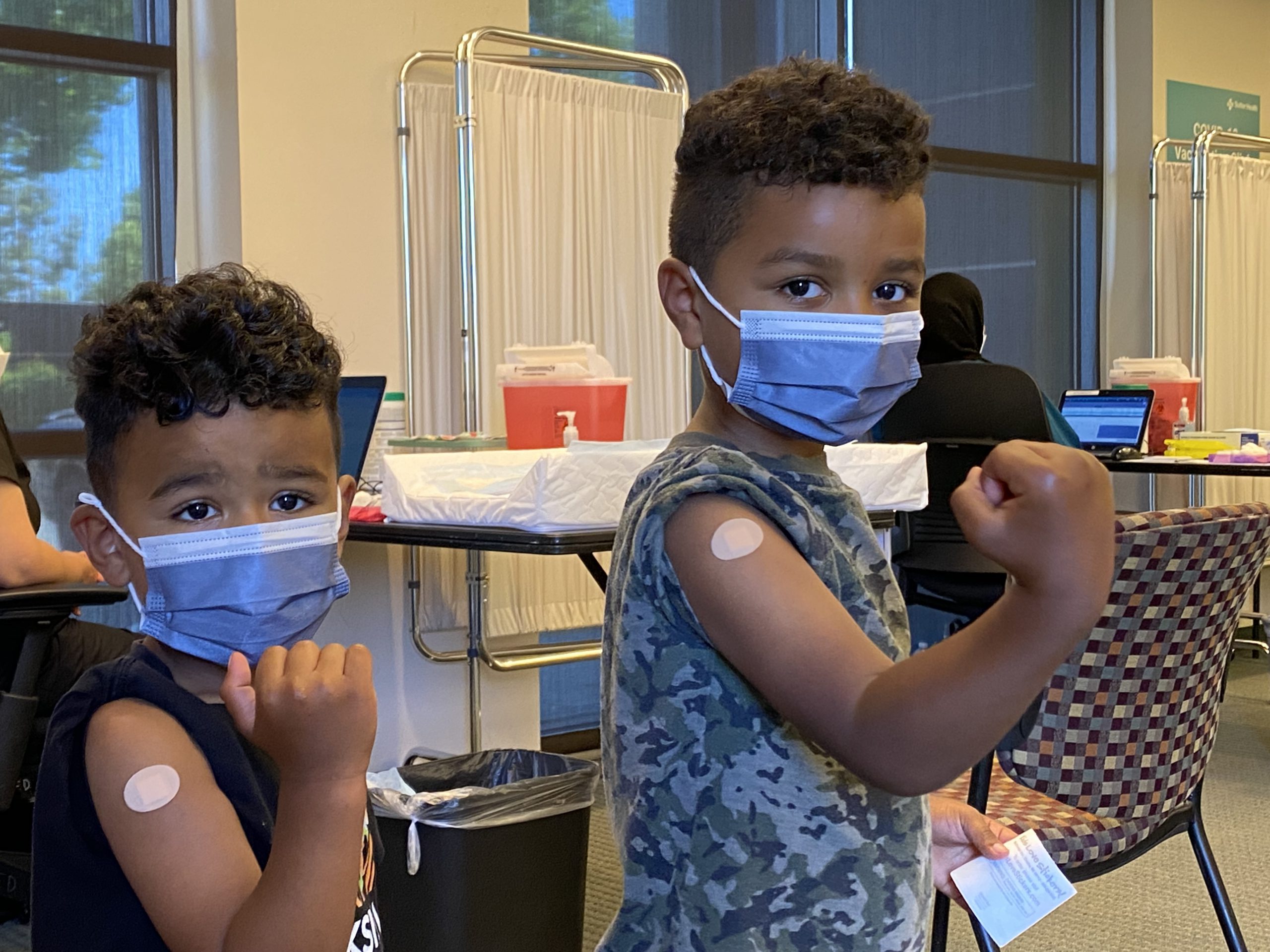 Two brothers make muscles with their biceps to display their strength after receiving their first dose of a COVID vaccine after it was newly approved at a Sutter Health vaccination clinic in the Bay Area. 