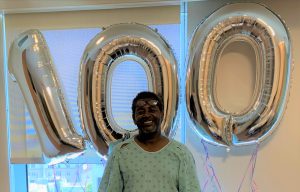 Brian White stands in front of balloons saying "100"