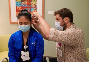 Nurse in uniform has acupuncture needles placed into her ear by a licensed professional