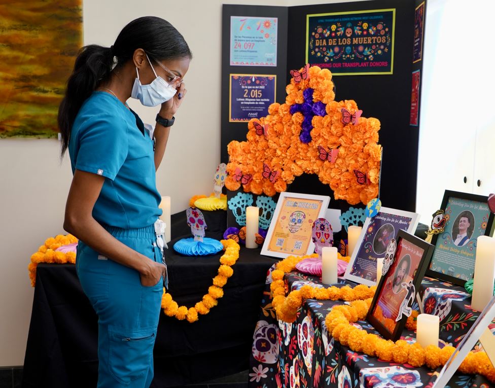 Nurse in teal scrubs wearing a masks visits a hospital's Day of the Dead display honoring people who have died and their organs were donated.