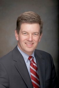 Portrait of Dr. Rob Nordgren, a Caucasian male in a grey suit with a red tie. 