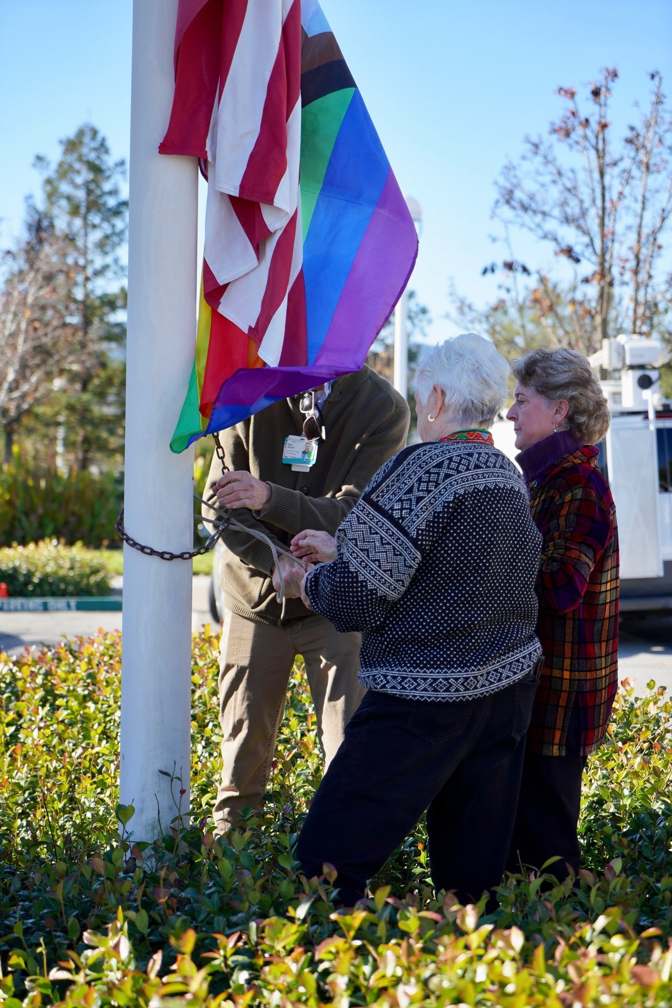Former Sutter patients Beth Reed and Lolma Olson work alongside a gentleman to hoist up a new rainbow flag underneath the American flag at Novato Community Hospital.