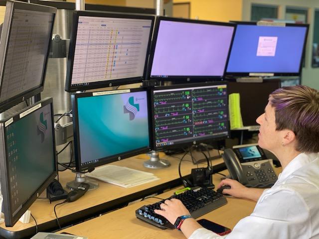 Female doctor in white coat looks at numerous computer screens