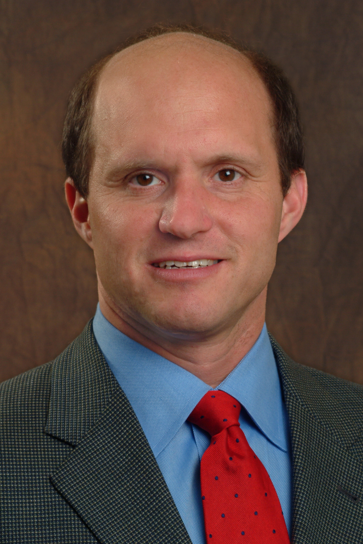A portrait of Dr. Jonathan Katz. He is a Caucasian male wearing a grey suit with a blue shirt and red tie. 