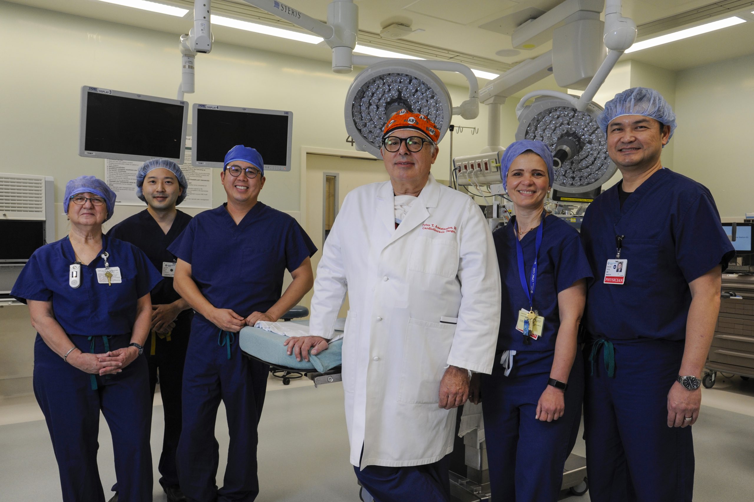 A doctor in white lab coat is flanked by his team in blue scrubs