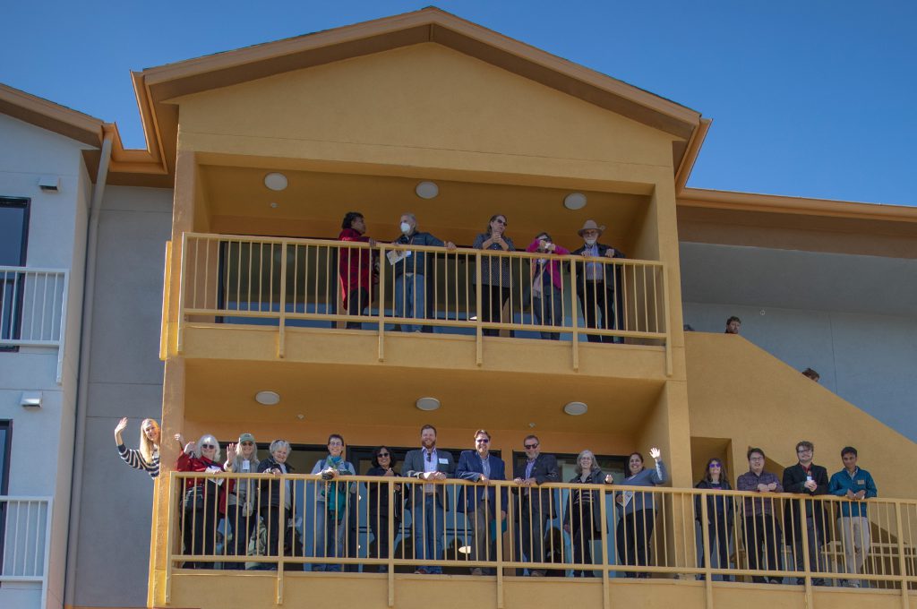 Numerous people waving from balconies of an apartment-style building.