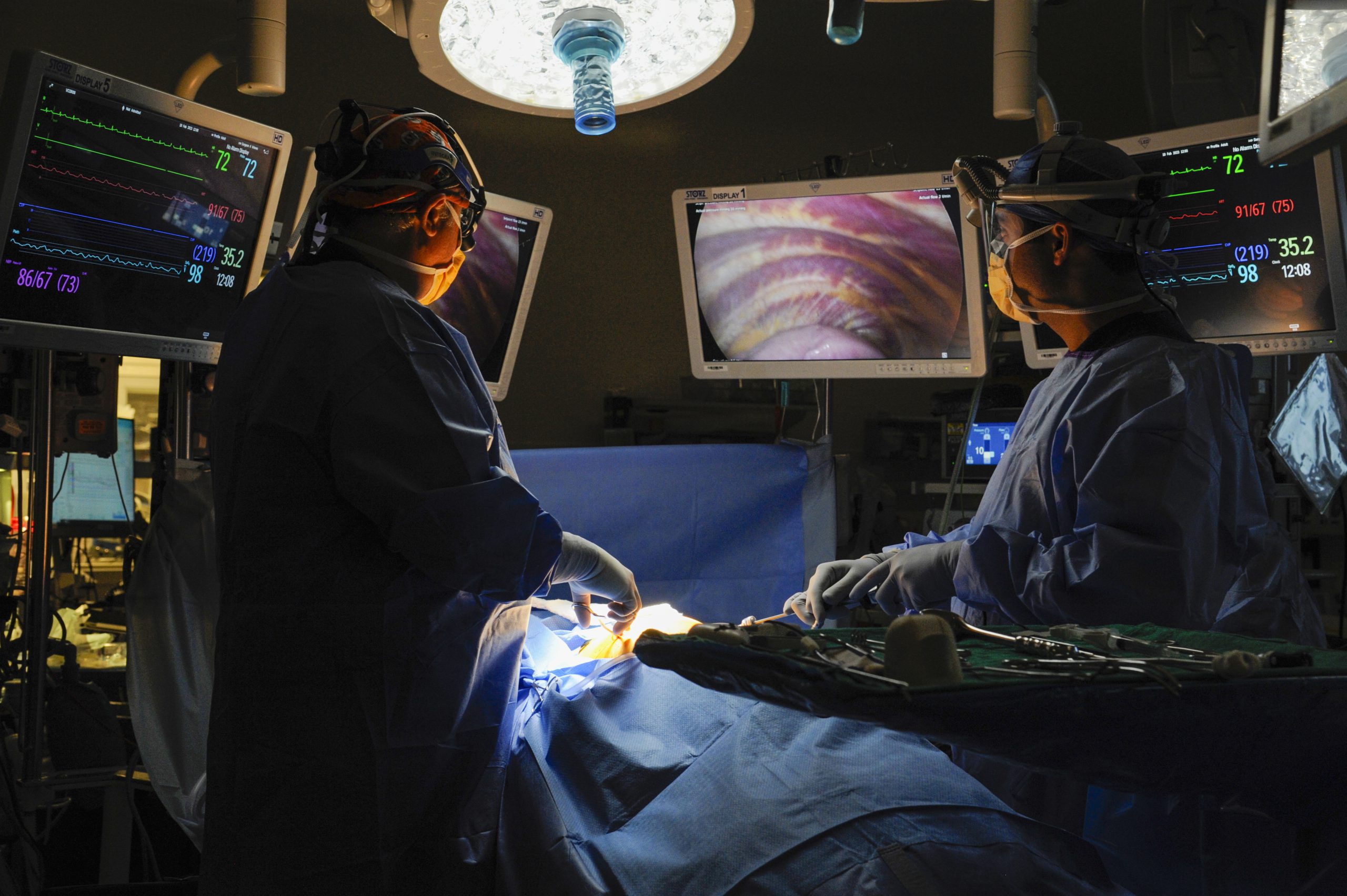 Surgeons operate on a patient while looking at computer screens.