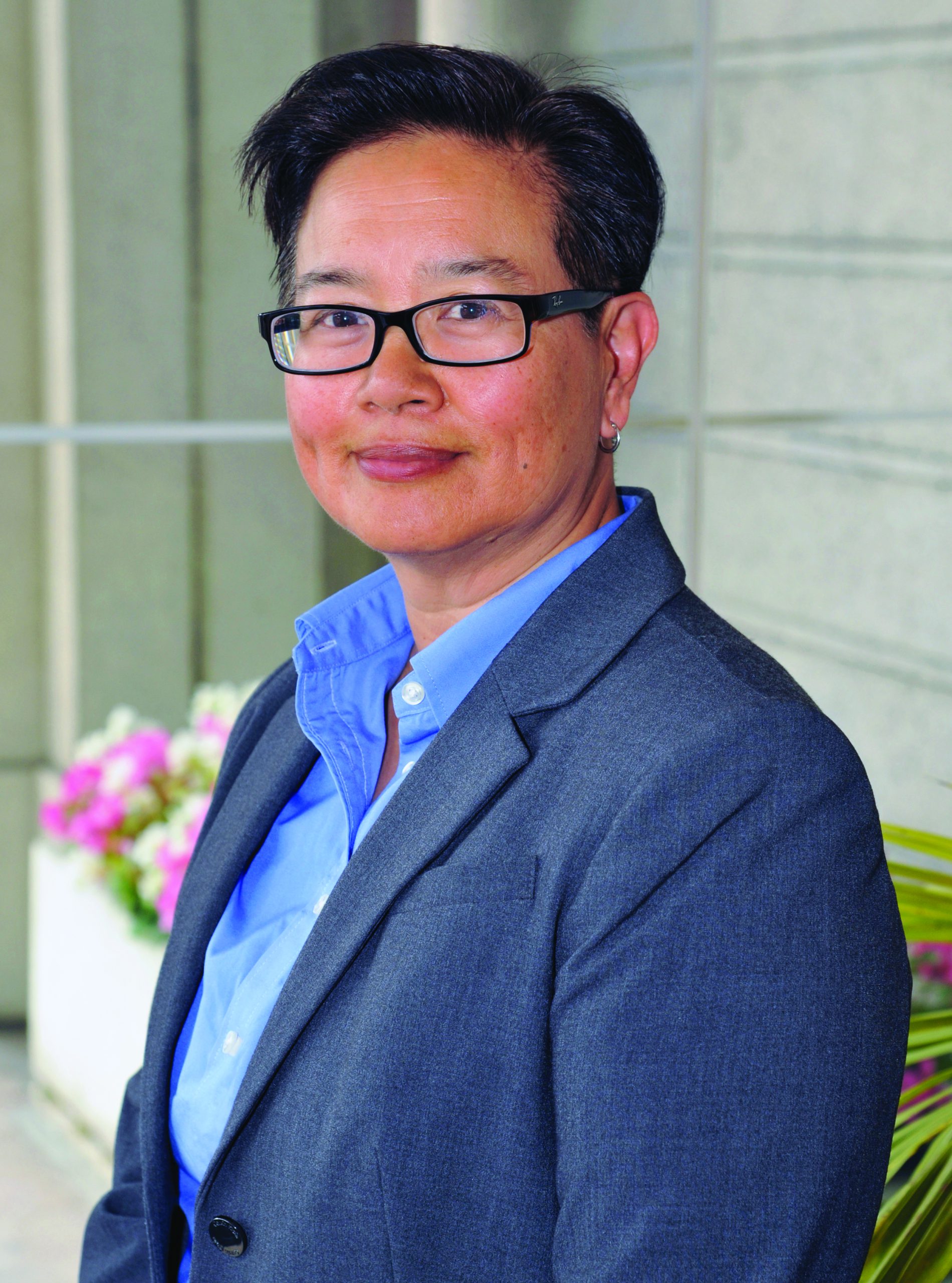 An Asian woman with short black hair stands in a blue shirt and suit jacket.