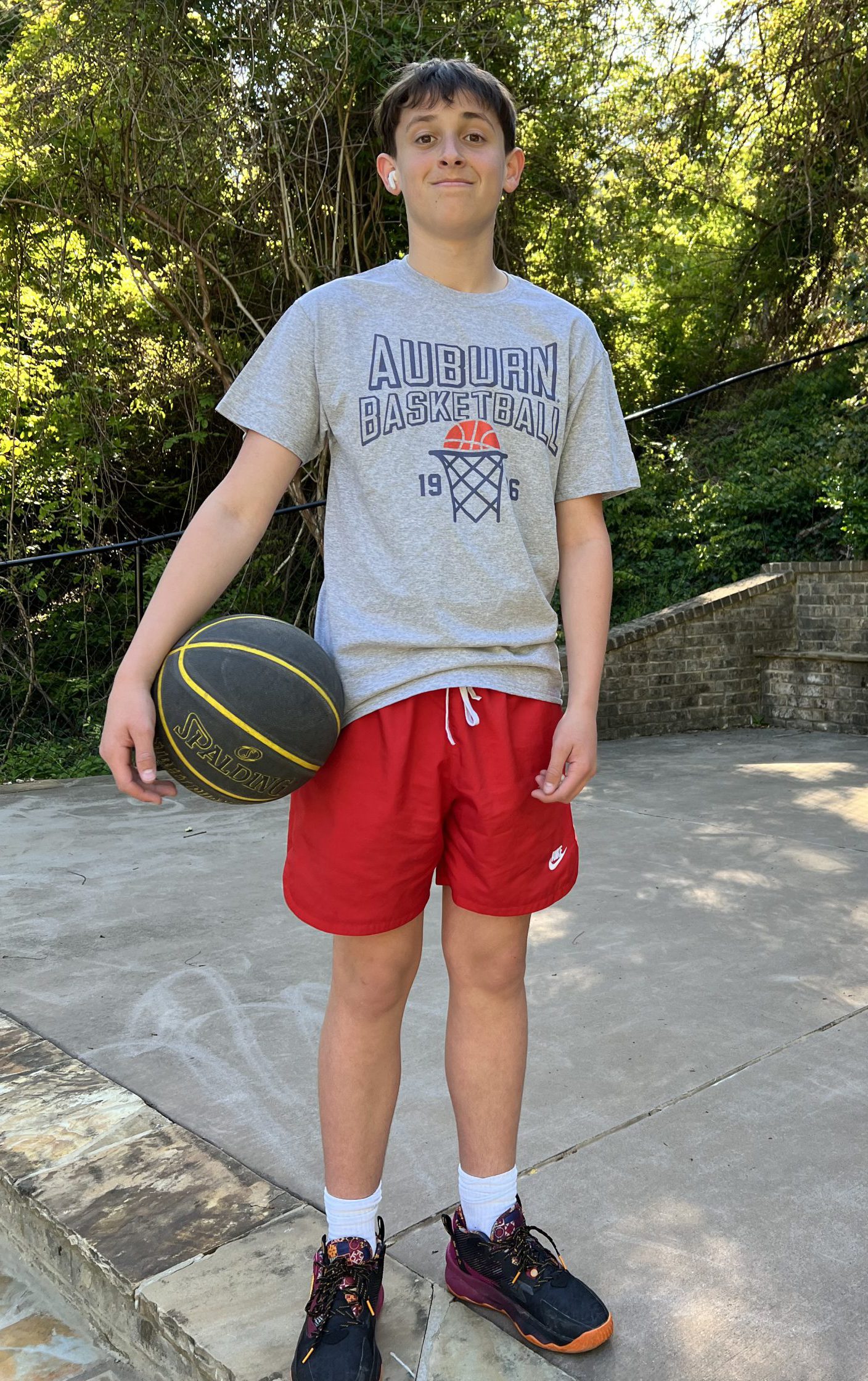 Caucasian teen with grey t-shirt and red shorts holds a black and yellow basketball.