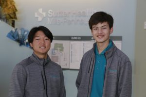 Two Asian teenage boys with zippered fleece jackets pose in front of hospital directory