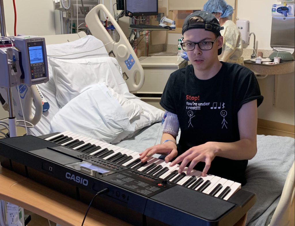 Teen plays a portable keyboard in a hospital room.