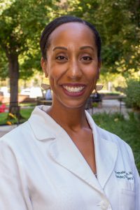 Black female physician with hair in bun with lab coat posing outdoors in park