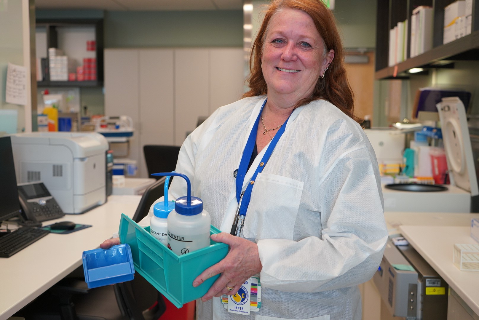 A Caucasian woman in a white lab coat holds lab materials in a clinical laboratory setting