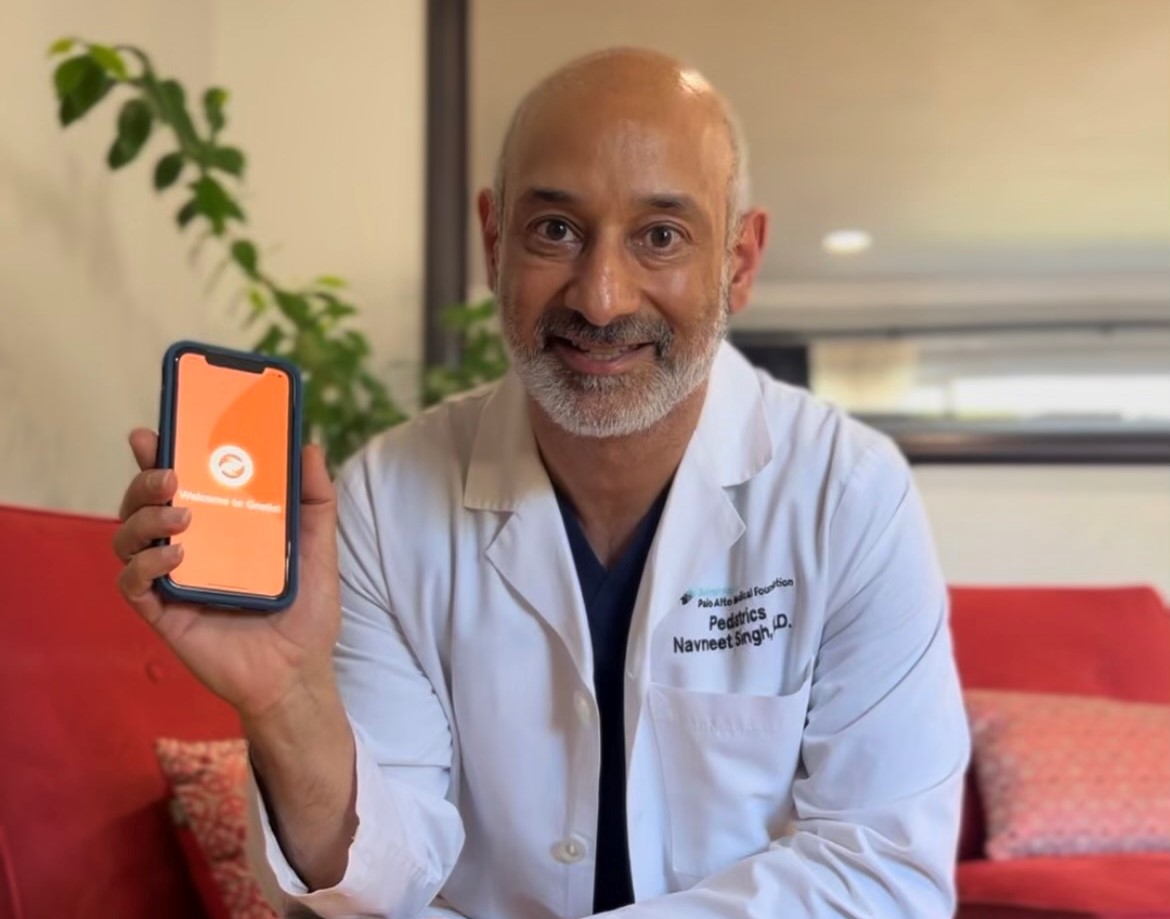 Dr. Navneet Singh holding a smart phone with the Gratis app logo on display.