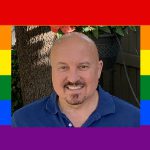 Caucasian bald man with dark goatee and blue polo shirt. Photo bordered with rainbow colors