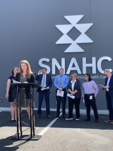 Red-haired woman shares remarks at a podium during a ribbon-cutting ceremony