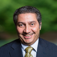 A middle-aged man who is Middle Eastern, wearing a blue suit and smiling