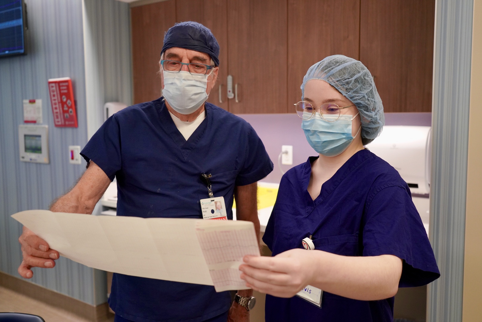 A doctor and student wearing scrubs review a patient's medical scan document. 